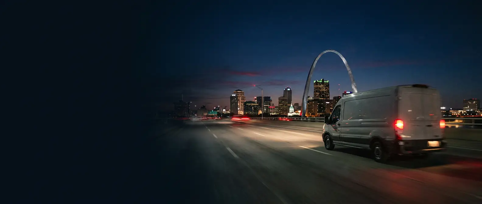 Delivery van crossing a bridge toward the St. Louis Gateway Arch at dusk